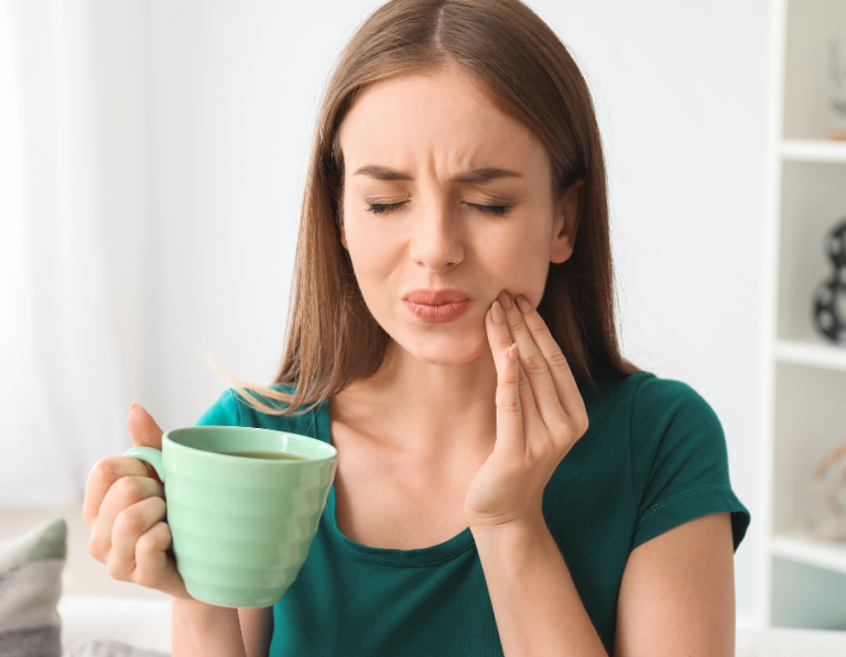 A woman wearing a green shirt holding a mug with coffee on the left and another hand in her cheek. In indoor setting.